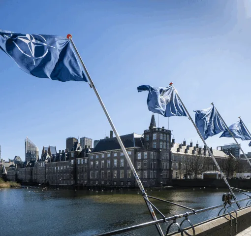 Rij blauwe NAVO-vlaggen langs de Hofvijver voor het Binnenhof in Den Haag onder een heldere blauwe lucht